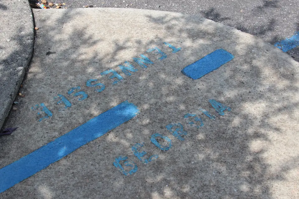 Painted blue stripe across a concrete sidewalk with stenciled 'TENNESSEE' and 'GEORGIA' on either side, in dappled shade