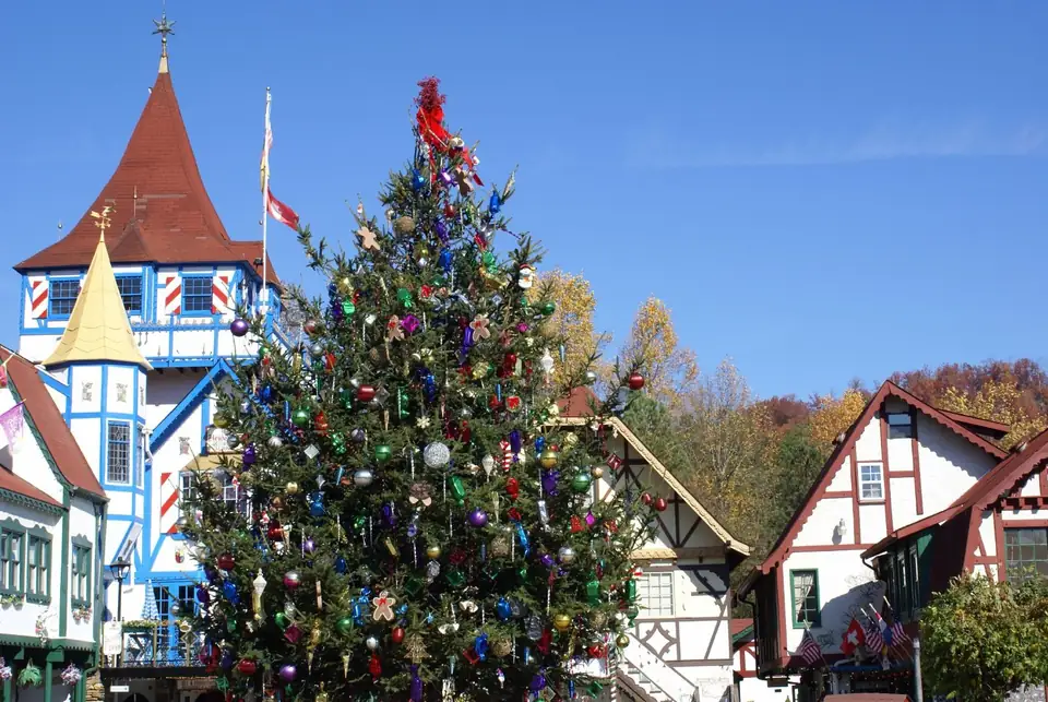 Tall decorated Christmas tree with colorful ornaments before half-timbered buildings and a red-roofed tower under blue sky